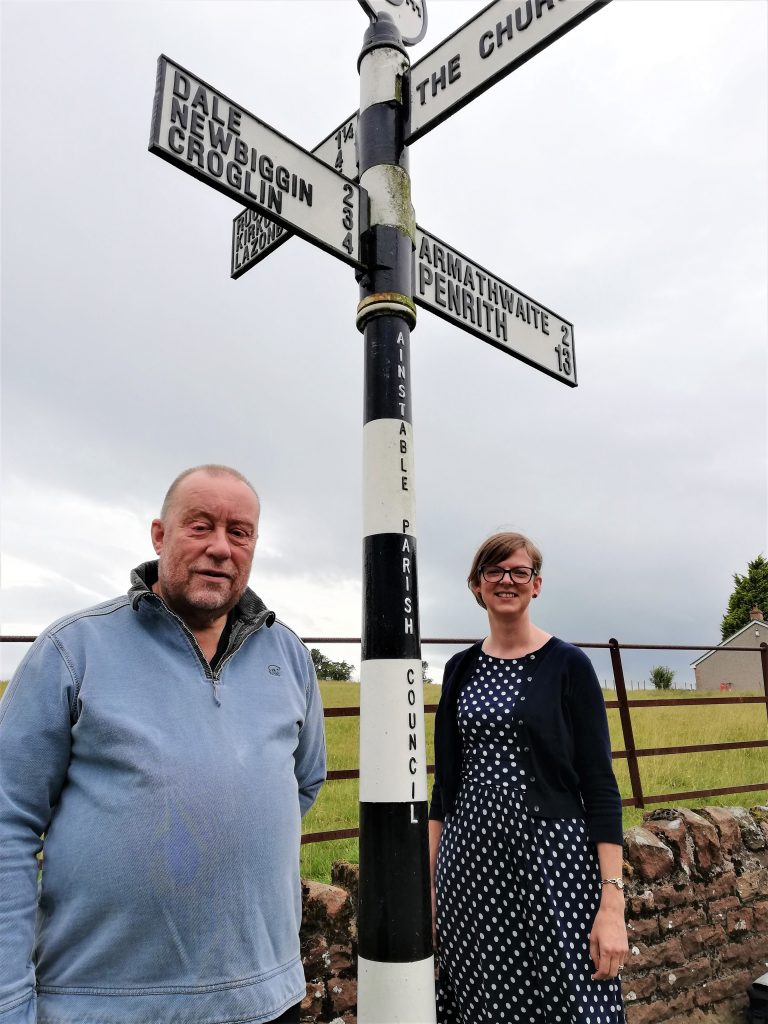 Chairman and Clerk stand bu signpost at Ainstable Crossroads.